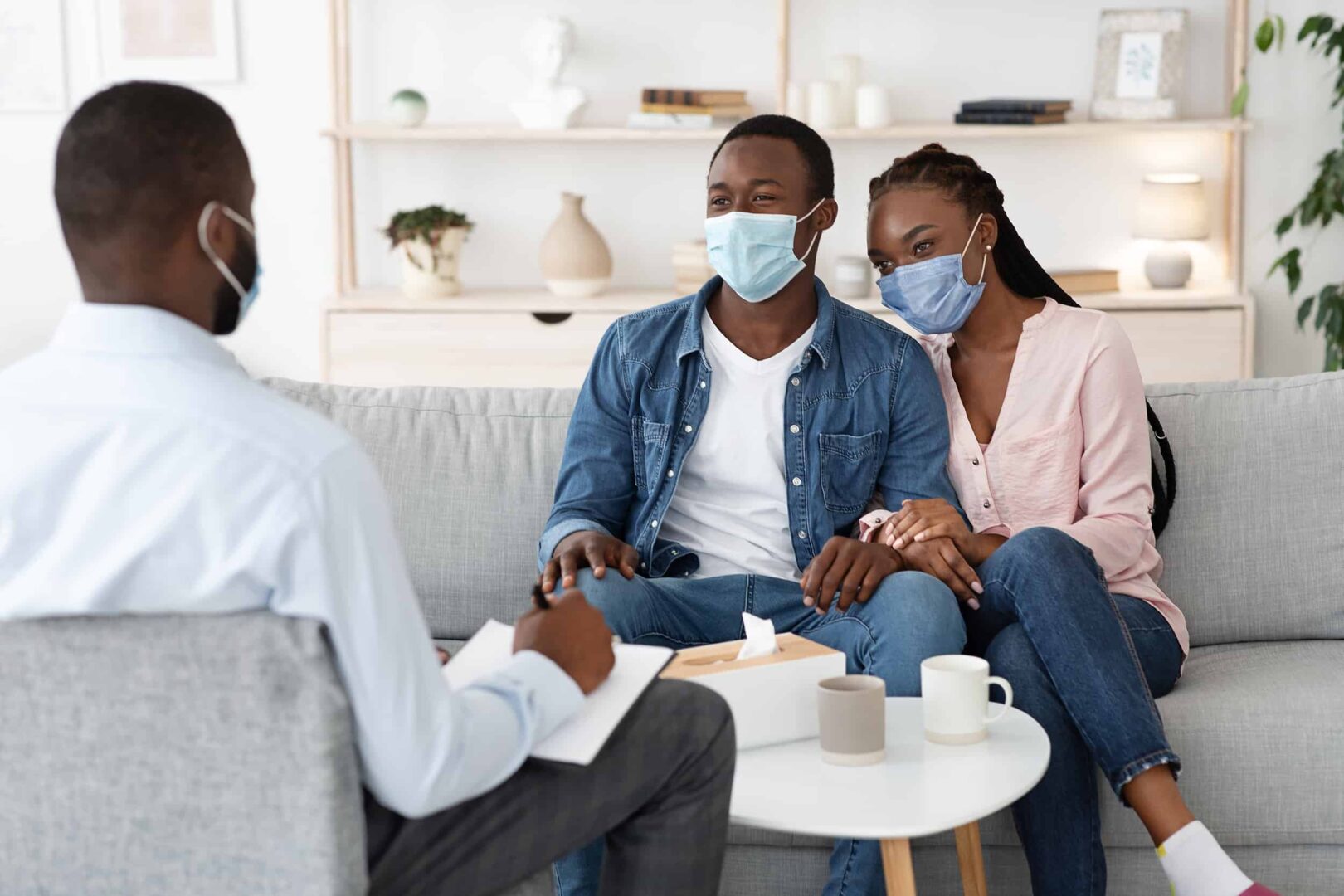 Terapia familiar durante la pandemia. Pareja negra con máscaras protectoras en la oficina del consejero