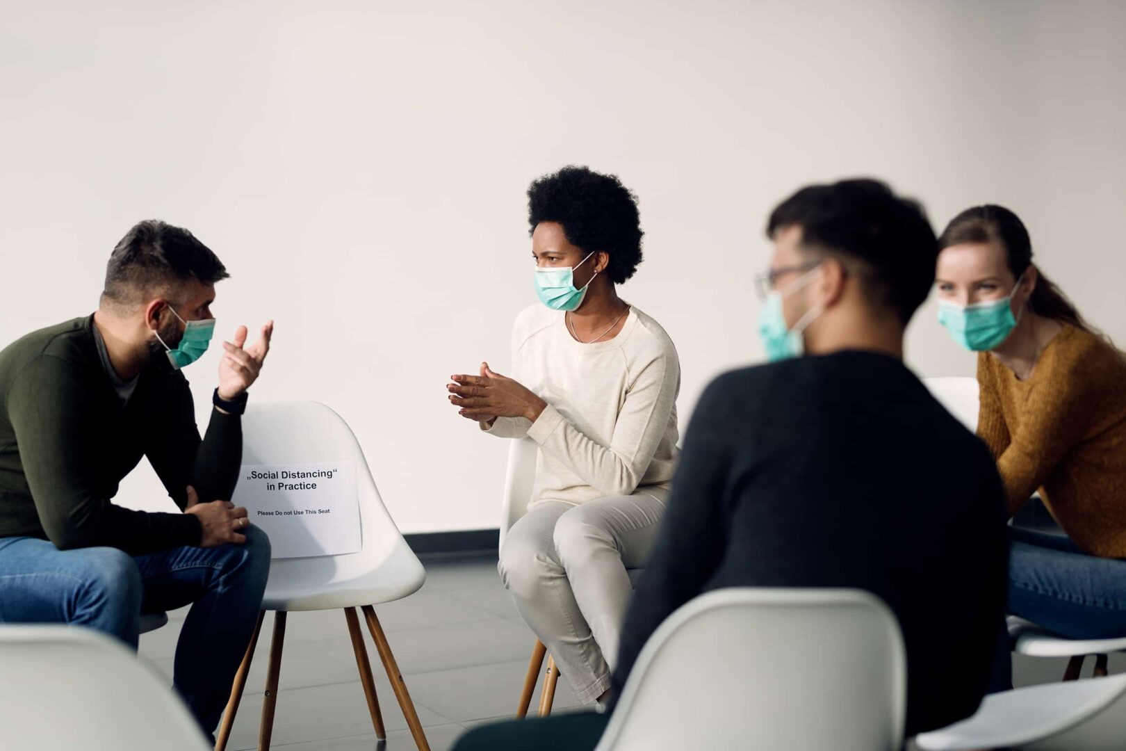 Grupo de personas con mascarillas protectoras mientras hablan durante una reunión de psicoterapia.