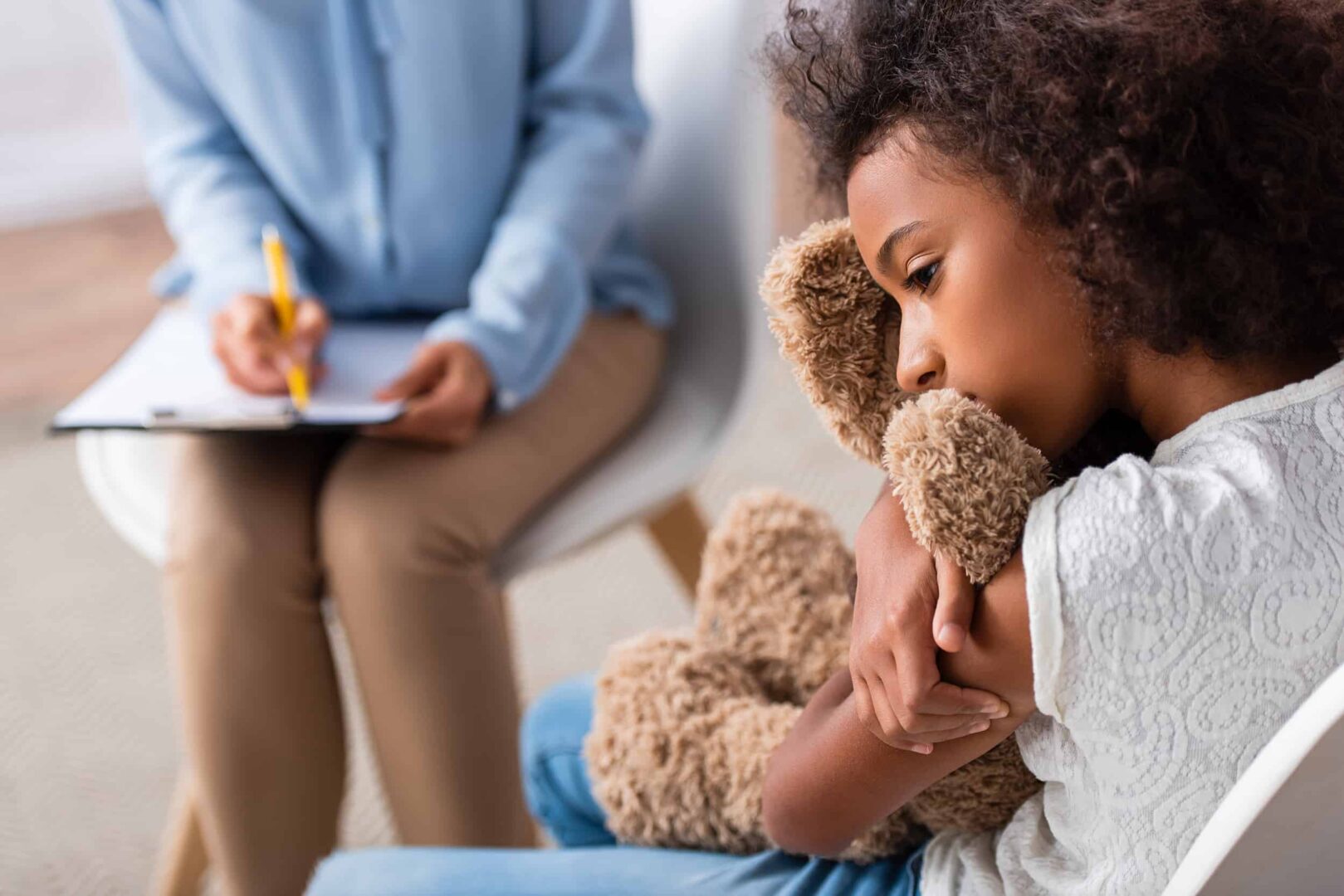 Niña afroamericana con autismo abrazando a un oso de peluche durante una fiesta