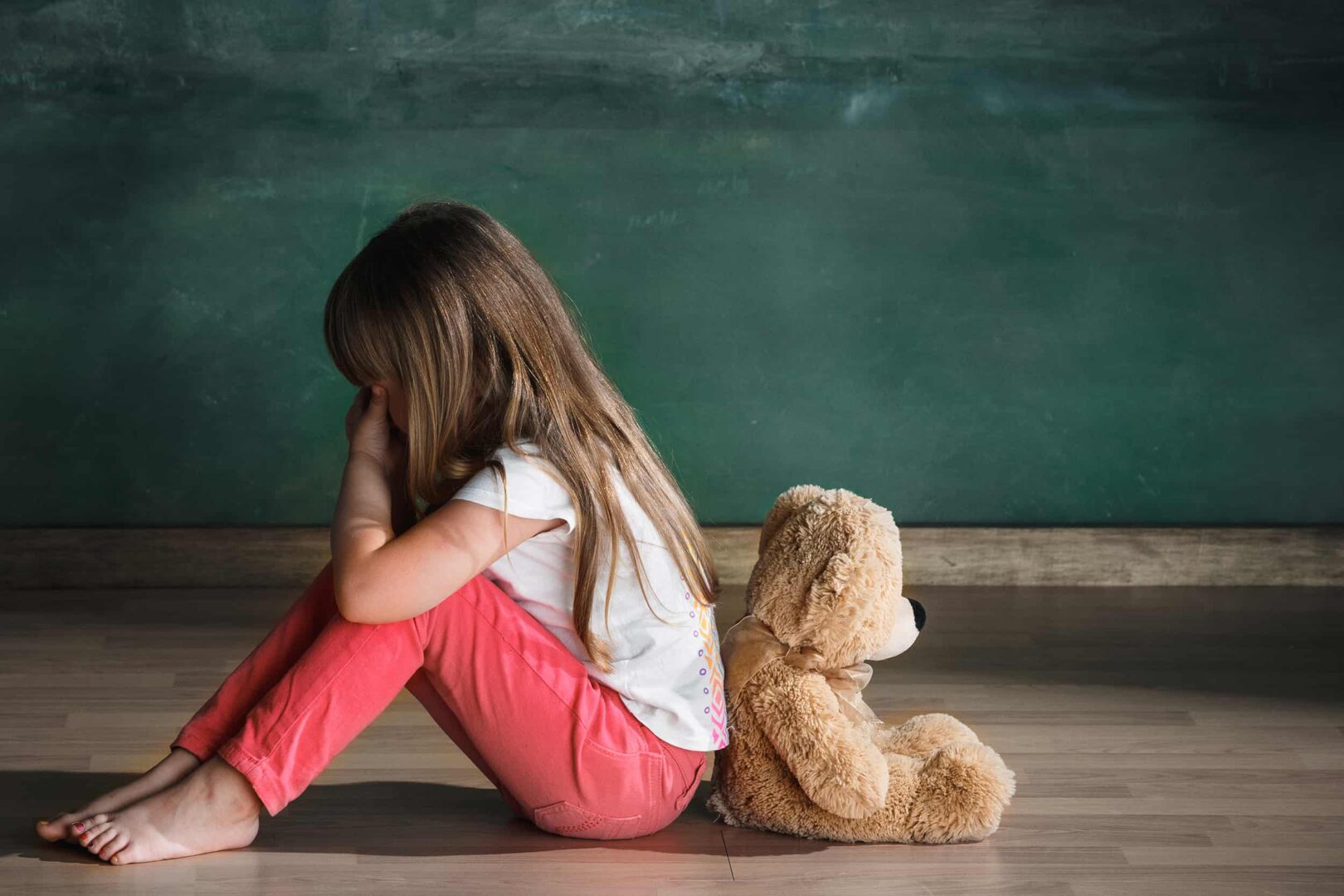 Niña con osito de peluche sentada en el suelo en una habitación vacía. Concepto de autismo